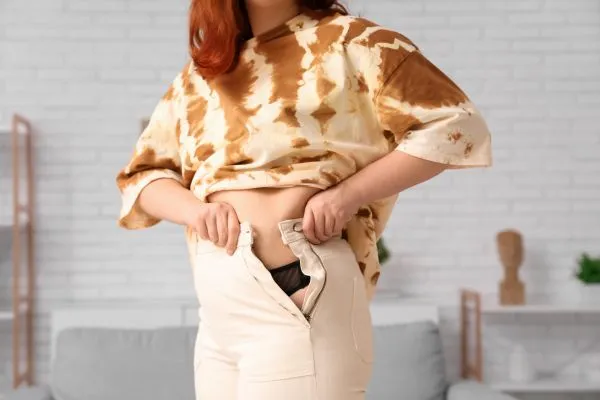 Image of woman trying to do her trousers up after pregnancy weight gain Bere Regis