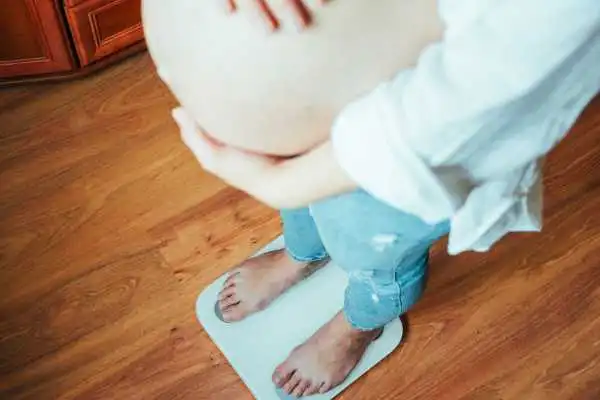 Image of woman weighing herself and experiencing weight gain through pregnancy Bere Regis